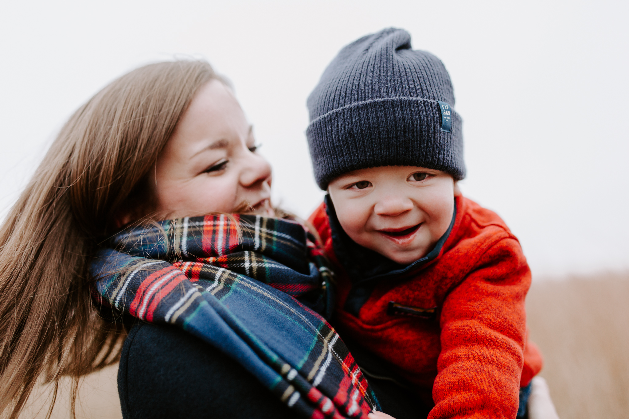 Mother in a plaid scarf swinging her young boy in her arms.